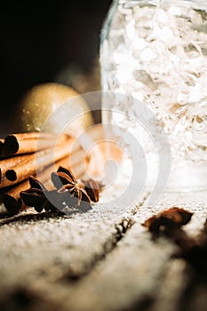 Christmas setting with bundle of cinnamon, jar with lights, anise stars and other christmas decorations on the rustic background