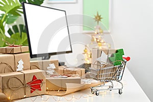 Christmas Shopping online. Christmas gifts and a computer monitor on a table in a home office.