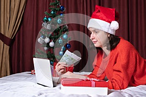 Christmas shopping online. A female customer places an order on a laptop in a decorated home interior
