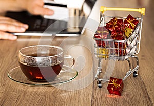 Christmas shopping online.  Thumbnail of a shopping trolley with laptop, bank card and glass of tea.  Concept.  Convenient shoppin