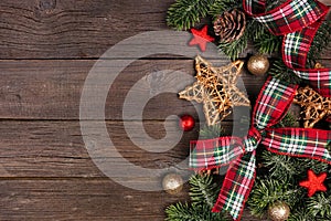Christmas side border of ornaments, branches and red and green plaid ribbon on a rustic wood background
