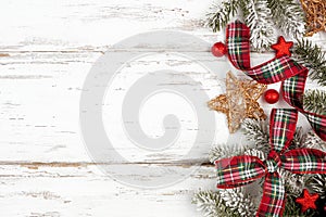 Christmas side border of ornaments, branches and red and green plaid bows and ribbon on a white wood background