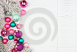 Christmas side border with pink, purple and teal ornaments and snowy branches, above view on a white wood background