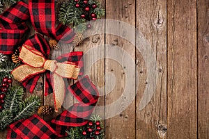 Christmas side border with red and black checked buffalo plaid ribbon, burlap and branches, overhead view on a wood background