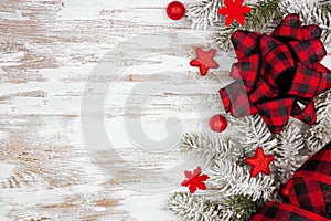 Christmas side border of ornaments, snowy branches and red and black check plaid bow and ribbon on a white wood background