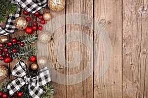 Christmas side border with white and black checked buffalo plaid ribbon, decorations and branches, overhead on a rustic wood backg