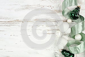 Christmas side border of white and frosty green ribbon and ornaments on a white wood background