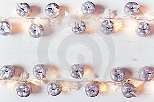 Christmas silver apples decoration and lights burning on a white wooden background.