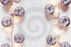 Christmas silver apples decoration and lights burning on a white wooden background.