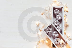 Christmas silver apples and lights burning in boxes on a wooden white background.