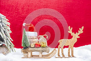 A christmas sled with presents, santa hat, fir tree and reindeer in the snow