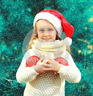 Christmas smiling child little girl in santa red hat with many balls near tree