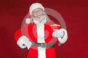 Christmas. Smiling, kind Santa Claus in white gloves holds a red bucket with popcorn with one hand, and puts the other