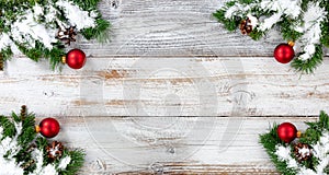 Christmas snow covered evergreen branches and red ball decorations in all corners on white vintage wooden boards