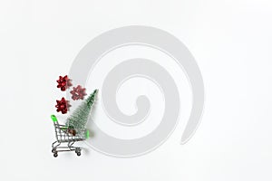 Christmas snow covered fir and red bows for gift in toy shopping cart on white background, copy space. New Year, sales, online
