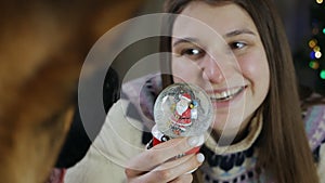 A Christmas snow globe in the hands of a young woman, shows it to the dog. Can be used as a Christmas or New Year gift