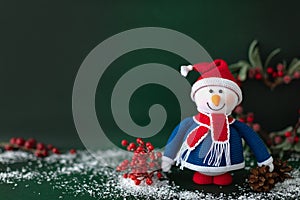 Christmas snow man standing with branch of winter berry and pines on dark green background