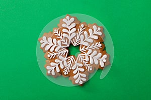 Christmas snowflake shaped gingerbread cookie on green background, top view