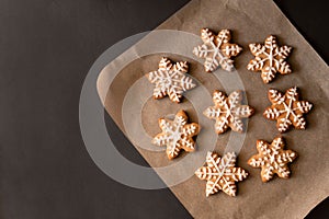 Christmas snowflake or star shape gingerbread cookie decorated with sugar icing on parchment on dark table background.