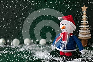 Christmas snowman in red hat and scarf standing in snow on dark green background