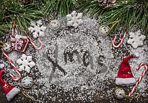 Christmas snowy background with the words x-mas Christmas candy, hat and pine branches and pine cone on wooden rustic background