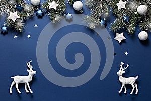 Christmas snowy border of shiny balls, stars and deer, evergreen branches on classic blue background