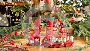 Christmas socks on the feet of a child on a background with golden bokeh. Socks decorated with fir branches with Christmas