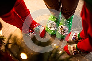 Christmas socks. Three pairs of foot, dressed in Xmas soks, stand around a tree. Atmosphere of Christmas.