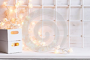 Christmas soft home decor with lights burning and boxes on a white wooden background.