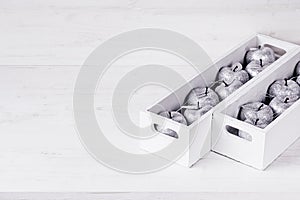 Christmas soft silver decorations in white boxes on a white wooden background.
