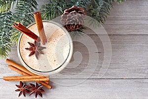 Christmas eggnog, top view with corner border of tree branches on gray wood