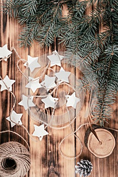 Christmas stars homemade cold porcelain garland with spruce branches on background of burnt wood, top view. Vertical