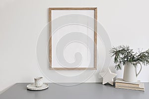 Christmas still life. Blank wooden picture frame mockup. Cup of coffee, pine tree branches in jug on grey table. Old