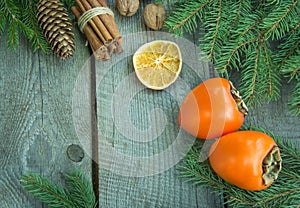 Christmas still life with fresh persimmon and cinnamon with pine tree on wooden background. Top view.