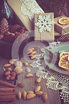 Christmas still life with giftbox, bowl with walnuts, almond, cinnamon, snowflakes on wooden table. Top view.