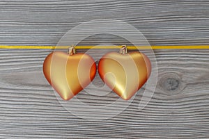 Christmas still life with love for loved ones, two golden hearts on one gold ribbon on a wooden background. Valentine`s Day Gift
