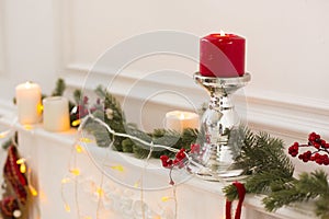 Christmas still life: metal candle holder with red burning candle, white candles, electric garland and green spruce branches photo