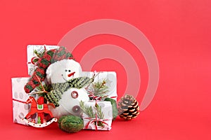 Christmas still life with snowman and gift boxes on a red background, decorated fir branches, pine cone and wooden decorations.