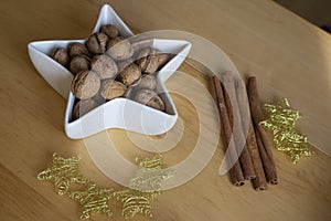 Christmas still life with walnuts in white bowl, golden thin wire stars and cinnamon bark decoration on wooden table