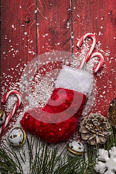 Christmas stocking with pine branches with cones, candy cane, on a red wooden background close up