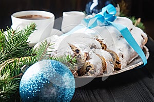 Christmas stollen on a silver tray with a white cup of hot coffee, a fur-tree branch Christmas toys, santaklaus and blue balloons