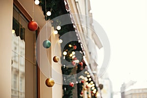 Christmas street decor. Stylish christmas fir branches with golden lights and colorful festive baubles in store window at holiday