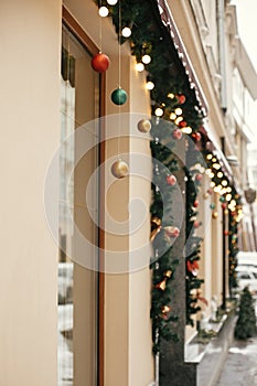 Christmas street decor. Stylish christmas fir branches with golden lights and colorful festive baubles in store window at holiday