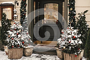 Christmas street decor. Stylish christmas trees with red and gold baubles and festive lights, covered with snow, at front of store