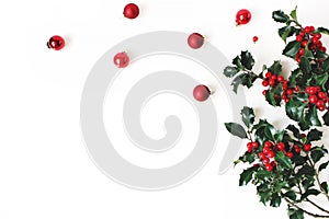 Christmas styled composition, decorative corner. Christmas glass balls, baubles and holly tree dark green leaves, red