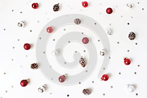 Christmas styled composition. Red Christmas glass balls, baubles, silver confetti stars and larch cones on white table