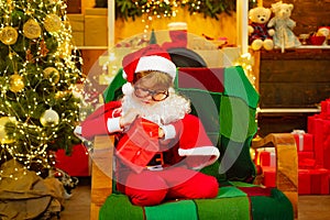Christmas surprise. The child opens a gift. Boy dressed as Santa Claus. Background for Christmas.