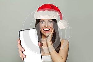 Christmas surprised brunette woman holding smartphone with empty blank display screen on white background