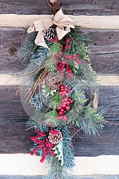 Christmas swag with pine, twigs, red berries, and burlap bow on wood wall