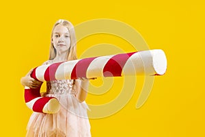 Christmas sweetness. A cute girl is holding a huge red and white candy cane sticking out her tongue against a yellow background.